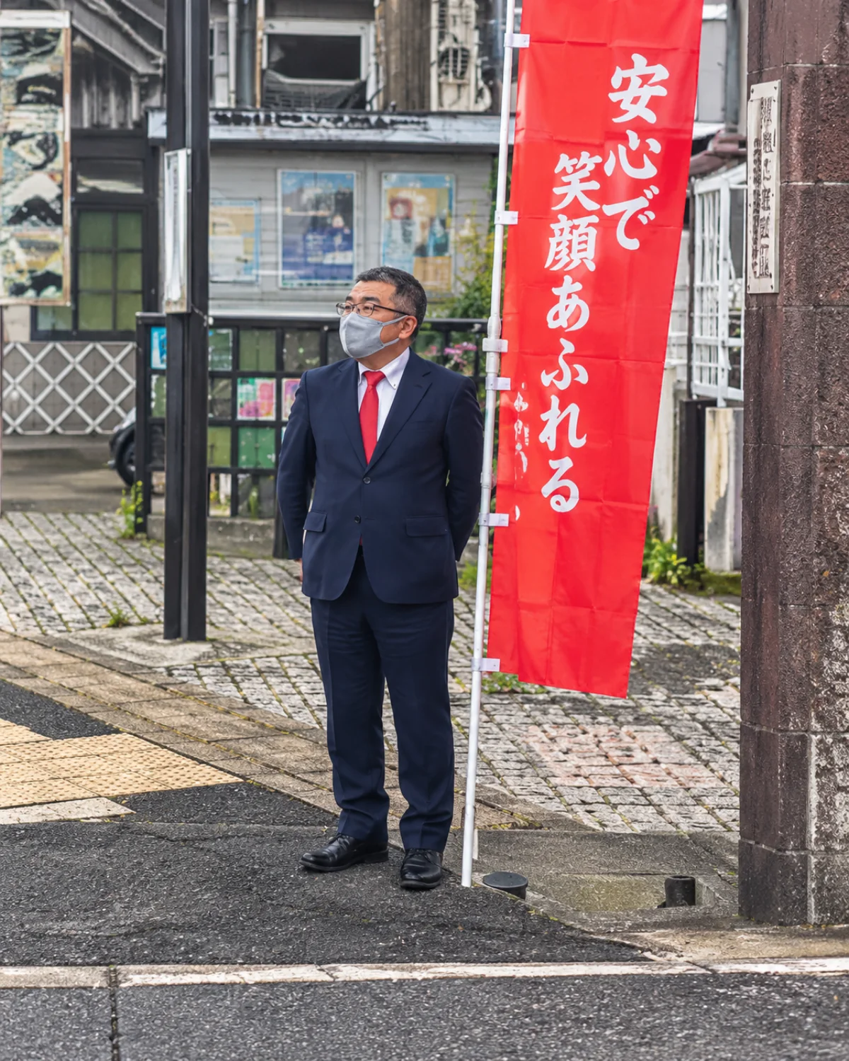 赤いのぼりとともに駅前に立つ鈴木たけし