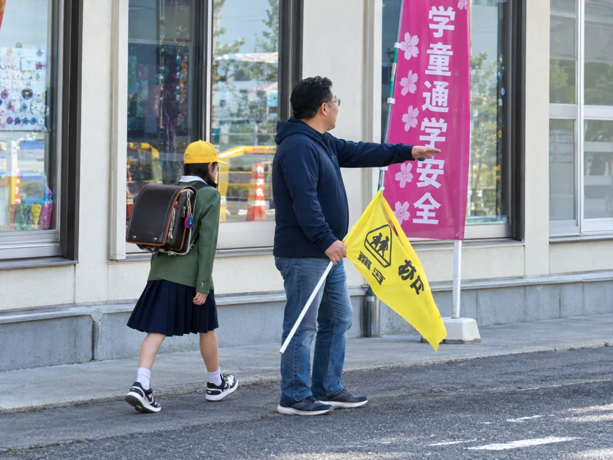 黄色い旗を持ち、登校する子どもを見守る鈴木たけし